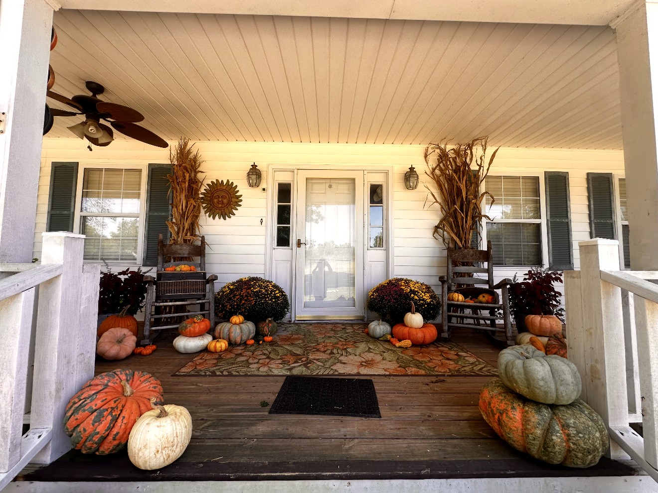 Styled front porch with rockers, mums, corn stalks, and heirloom pumpkins